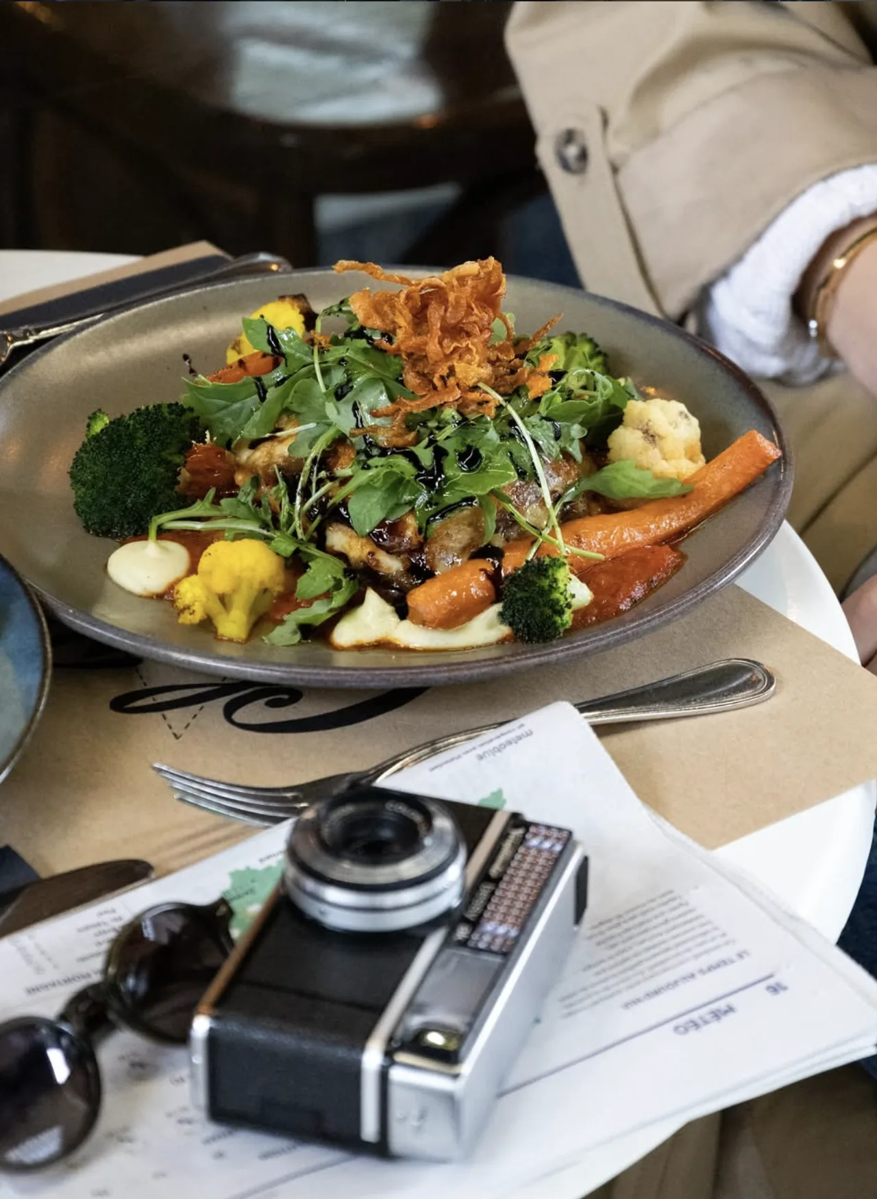 Une assiette de poisson et légumes rôtis, roquette et oignons frits, posée sur une table de la salle.
